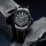 Maurice Lacroix AIKON-IC Frozen Carbon ambientazione su acciaio damasco, dettaglio lunetta ceramica nera e indici luminosi AC6008-K1C34-130-3